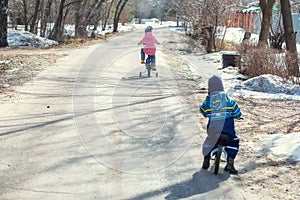 Children ride a bicycle and a runbike along the village road