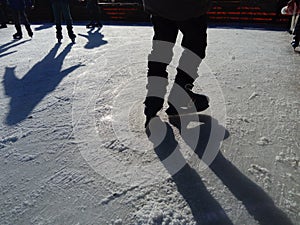 Children ride in a city park on an ice rink. Feet skater while skating on ice. The low winter sun weakly illuminates the