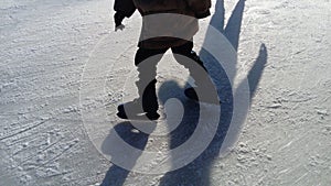 Children ride in a city park on an ice rink. Feet skater while skating on ice. The low winter sun weakly illuminates the ice. Dark