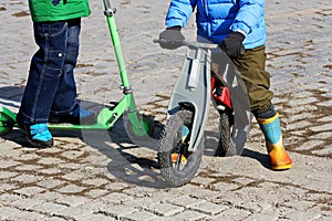 Children ride on a scooter and a balance bike.