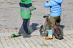 Children ride on a scooter and a balance bike.