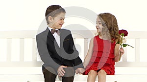 Children ride a swing and a little boy kisses the girl on the cheek. White background