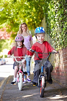 Children Riding Bikes On Their Way To School With Mother