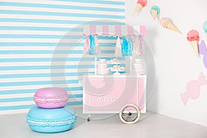 Children room with blue stripe background. candy stall photo zone with big macaroons, sweets and marshmallows. trolley with ice cr