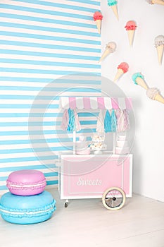 Children room with blue stripe background. candy stall photo zone with big macaroons, sweets and marshmallows. trolley with ice cr