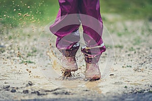 Children in rubber boots and rain clothes jumping in puddle.