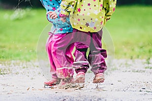 Children in rubber boots and rain clothes jumping in puddle.