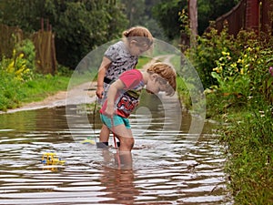 children in rubber boots with toys on a rope in a deep pool after a rain peer into the water