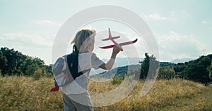 Children run holding toy aircraft on mountain meadow at summer vacation