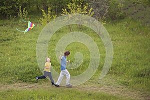 Children run playing kite on summer meadow