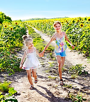 Children running across sunflower field outdoor.