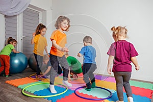 Children running and jumping around multicolor hoops on a floor