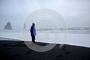 Children running from and to the ocean in black sand beach of Reynisfjara and the mount Reynisfjall in Iceland on a cold rainy day