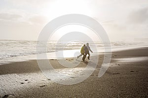 Children running from and to the ocean in black sand beach of Reynisfjara and the mount Reynisfjall in Iceland on a cold winter