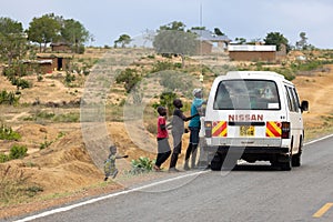 Children running towards a car on a Kenyan road, hoping for sweets from passing drivers