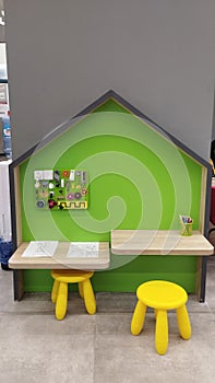 a children\'s area in the form of a house in a store with two wooden tables for drawings, two yellow stools