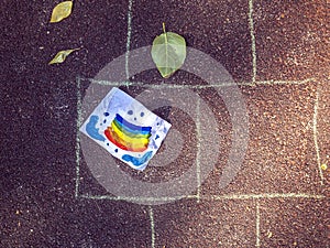 Children`s art creativity. Drawing rainbow on papaer sheet on asphalt. Crumpled sheet with kid`s drawing