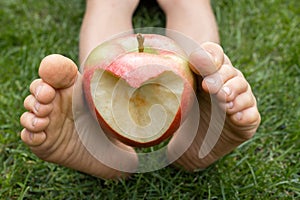 children's bare feet hold an apple with a heart carved in it