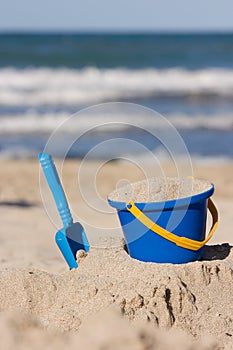 Children`s beach toys - bucket and shovel on sand on a sunny day. Outdoor kid`s activities at a beach with sea waves