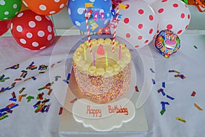 Children`s Birthday cake with candles set in front of colourful spotty ballons