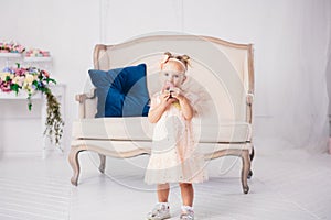 Children`s birthday. funny two-year-old Caucasian girl in pink dress standing to bedroom of house the background of couch and eat