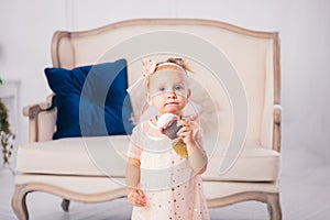 Children`s birthday. funny two-year-old Caucasian girl in pink dress standing to bedroom of house the background of couch and eat