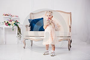 Children`s birthday. funny two-year-old Caucasian girl in pink dress standing to bedroom of house the background of couch and eat