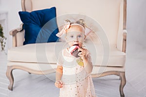 Children`s birthday. funny two-year-old Caucasian girl in pink dress standing to bedroom of house the background of couch and eat