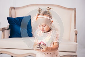 Children`s birthday. funny two-year-old Caucasian girl in pink dress standing to bedroom of house the background of couch and eat