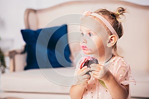 Children`s birthday. funny two-year-old Caucasian girl in pink dress standing to bedroom of house the background of couch and eat