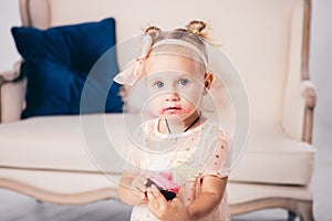 Children`s birthday. funny two-year-old Caucasian girl in pink dress standing to bedroom of house the background of couch and eat