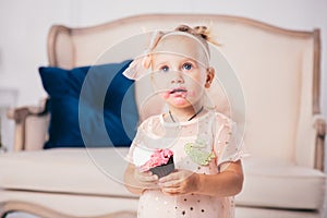 Children`s birthday. funny two-year-old Caucasian girl in pink dress standing to bedroom of house the background of couch and eat