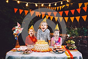 Children`s birthday party. Three cheerful children girls at the table eating cake with their hands and smearing their face. Fun a