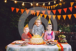 Children`s birthday party. Three cheerful children girls at the table eating cake with their hands and smearing their face. Fun a