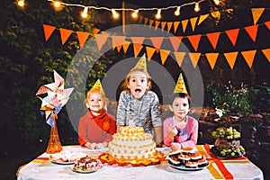 Children`s birthday party. Three cheerful children girls at the table eating cake with their hands and smearing their face. Fun a