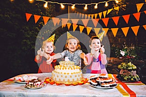 Children`s birthday party. Three cheerful children girls at the table eating cake with their hands and smearing their face. Fun a