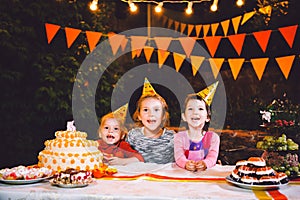 Children`s birthday party. Three cheerful children girls at the table eating cake with their hands and smearing their face. Fun a