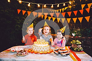 Children`s birthday party. Three cheerful children girls at the table eating cake with their hands and smearing their face. Fun a