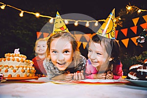 Children`s birthday party. Three cheerful children girls at the table eating cake with their hands and smearing their face. Fun a