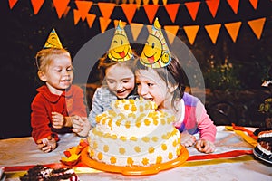 Children`s birthday party. Three cheerful children girls at the table eating cake with their hands and smearing their face. Fun a