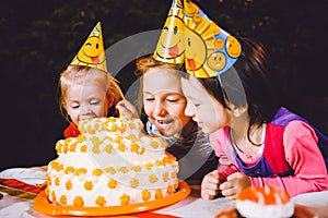 Children`s birthday party. Three cheerful children girls at the table eating cake with their hands and smearing their face. Fun a