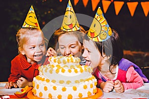 Children`s birthday party. Three cheerful children girls at the table eating cake with their hands and smearing their face. Fun a