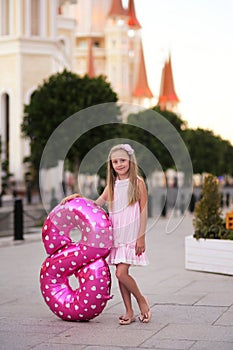 Children`s birthday. Smiling a beautiful blond little girl with a helium ball in the form of a figure eight celebrates her