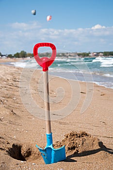 Children`s blue and red shovel, hammered into the sand on the beach