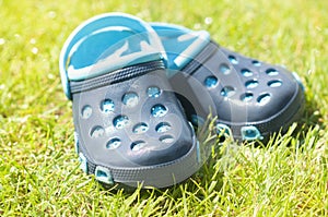 Children`s blue slippers on the green grass in the garden, shoes for children, beach fashion for kids, a concept of