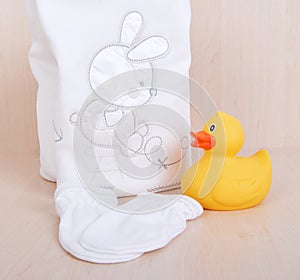 Children`s clothing diapers pajamas mittens socks vests sliders white background and ruber toy yellow duck