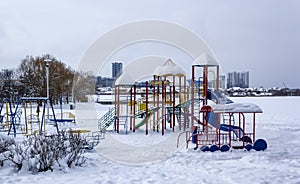 Children`s colorful playground in the snow on the lake in the city park