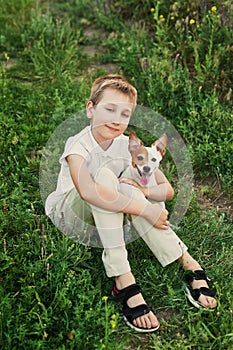 Children`s Day. Happy little child boy having fun with dog pet Jack Russell Terrier on field. Summer walk. Childhood concept.