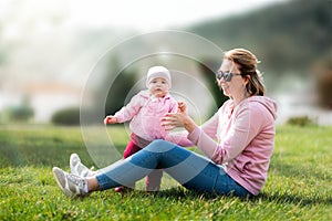 Children`s day. A young mother is sitting on the grass, playing with her baby. Recreation in the park with a child. Blurred