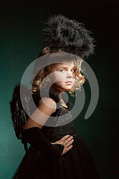 Children`s demon with black wings costume in carnival and religious style in the studio with an interesting emotion.